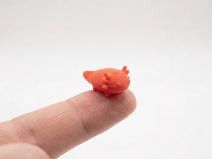 A tiny pink printed axolotl on a fingertip.