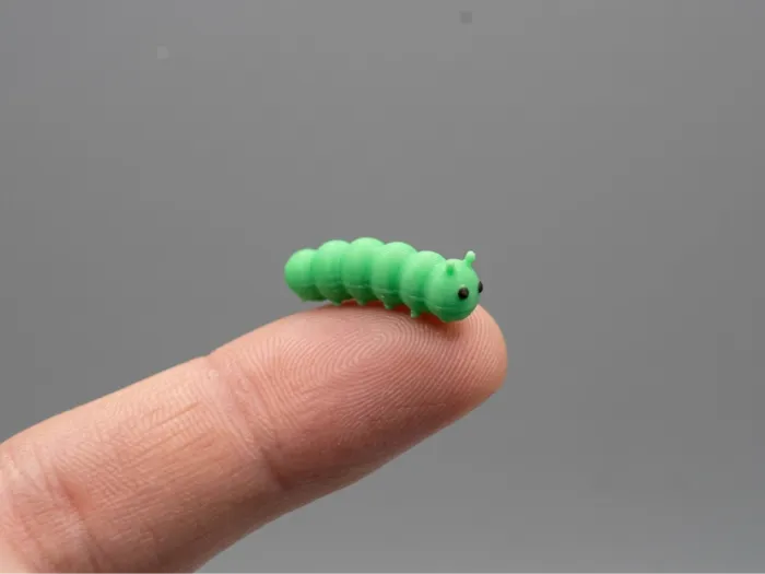 A tiny green printed caterpillar on a fingertip.